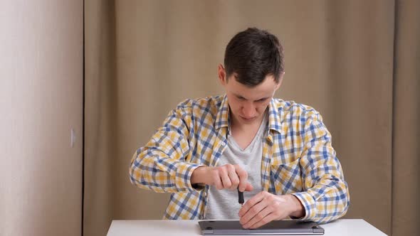Young Man Disassembles a Laptop with a Screwdriver While Sitting at Table