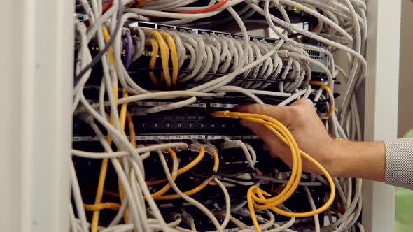 Male IT Technician Working On  Switch Router Standing Open Server Rack Cabinet in Big Data Center.