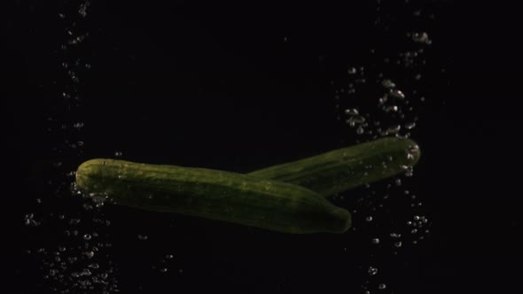 Cucumbers Falling Into Water with Bubbles on Black Background. Vegetables Falling Into Water on