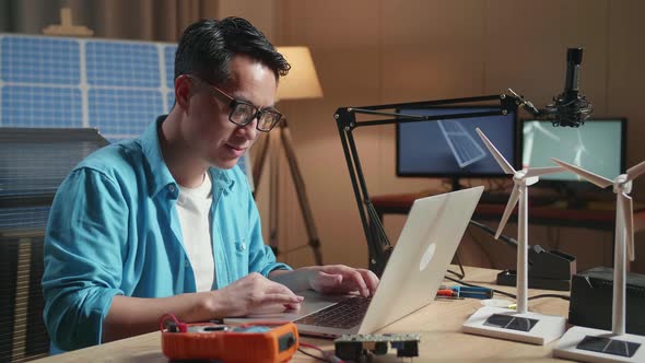 Asian Man Sitting In Front Of Solar Cell Typing On A Laptop At The Office