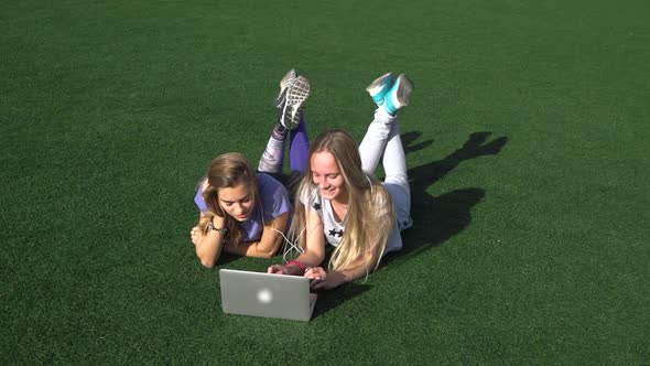 Two Girls Are Lying on the Lawn with Grass Using Laptop