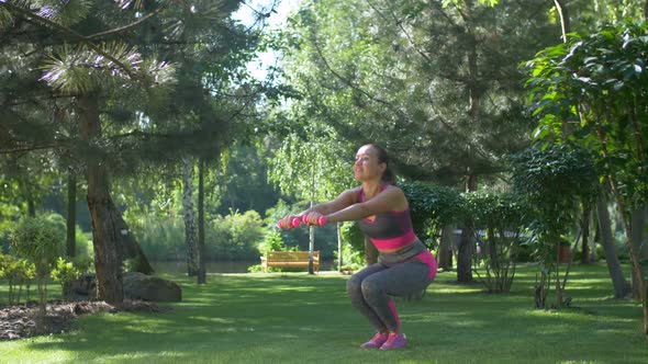 Fitness Female with Dumbbells Squatting Outdoors