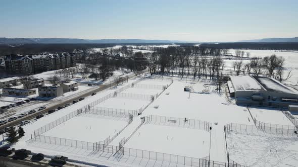 View toward the snow and ice covered river in winter. Park with tennis courts covered in snow.