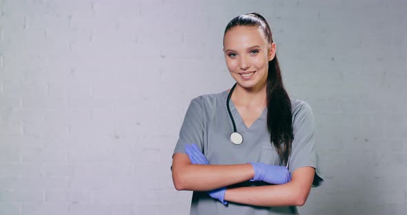 Portrait of Glad Smiling Doctor in White Uniform Standing with Crossed Hands on Gray Background