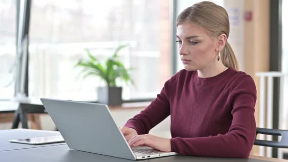 Young Woman with Laptop Smiling at Camera in Office