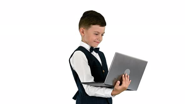 Smiling Boy in a Bow Tie and Waistcoat Using Laptop Computer While Standing on White Background