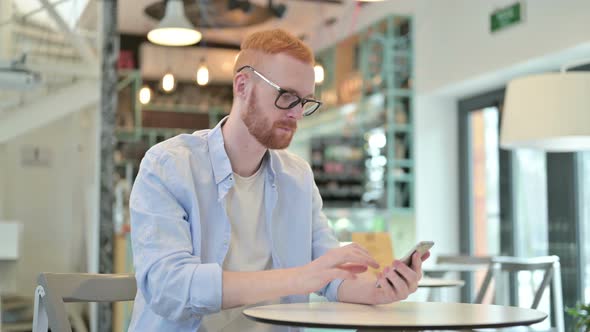 Focused Redhead Man Using Smartphone in Cafe 