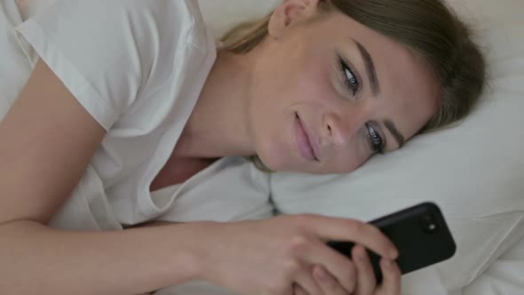 Portrait of Attractive Young Woman Using Smartphone in Bed