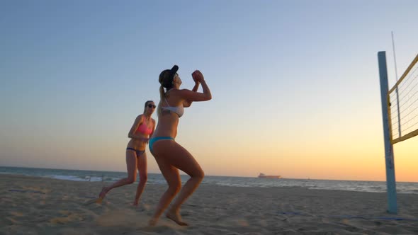 Women players play beach volleyball at sunset and a player hand sets the ball.