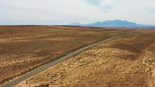 Car driving down a hot desert road with mountain background in Utah, USA - Aerial flying over view