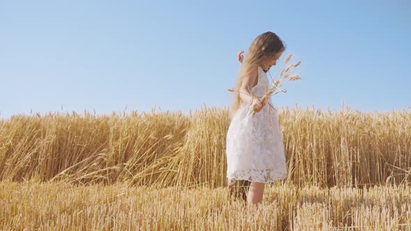 Cheerful Girl Dances in Wheat Field Holding Spikelet Bouquet