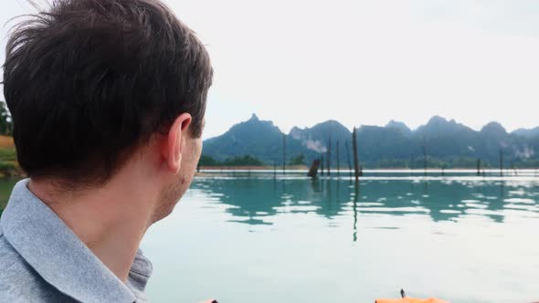 CloseUp of Smiling Man Sitting on Boat and Sailing on Morning Lake with Mountain