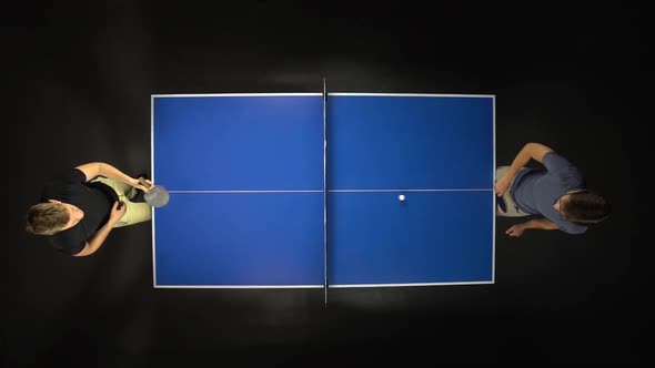 Two Young Men Playing Ping Pong Game Enjoying Competitive Sport in Dark Background. Top View. Slow