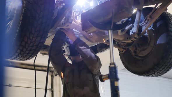 Gas Electric Welder Welds the Rear Suspension Part of an SUV