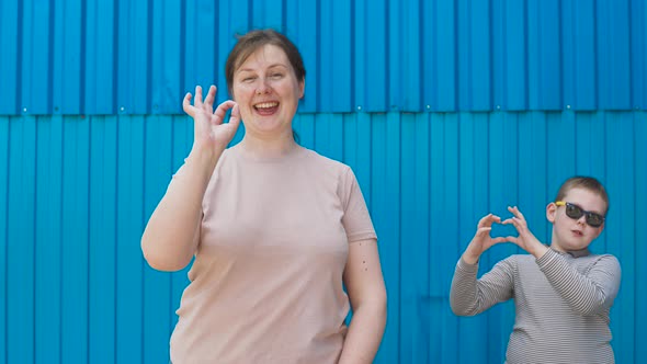 Mom and Son Show Popular Gestures to Camera Against Bright Blue Wall