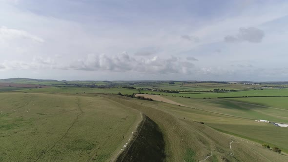 Aerial tracking slowly west above the northern ramparts of Maiden Castle. Beautiful green fields and