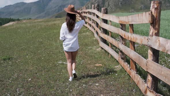 A Young Woman in Shorts and a White Shirt Walks Along a Fence in Rural locality.Attractive Brunette