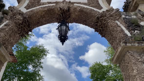 Look up of arch with lamp agains blue and cloudy sky. Beautiful architectural details