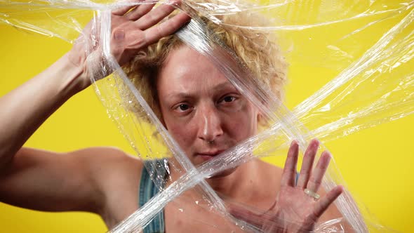 Young Androgynous Man Putting Head in Cling Film Looking at Camera