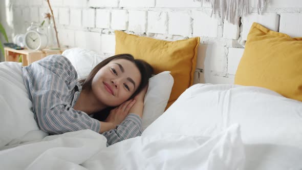 Portrait of Cute Asian Girl Lying in Bed Awake Wearing Pajamas Smiling and Looking at Camera