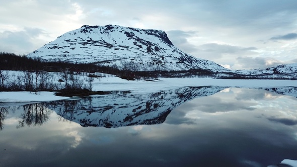 Winter Norwegian landscape with snowy mountains and fjord. Reflection of the mountain in the water.