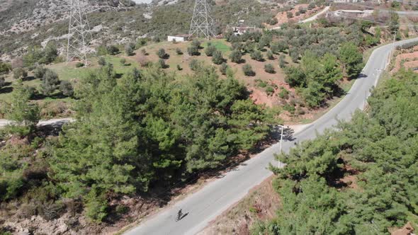 Triathlete is climbing to mountain pass on road bicycle on empty car road, pedaling out of saddle 