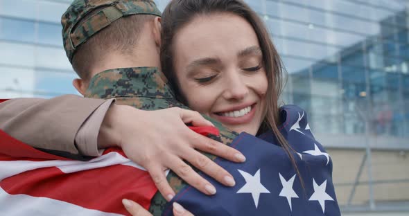 Happy Girl Embracing Military Boyfriend Covered with American Flag.