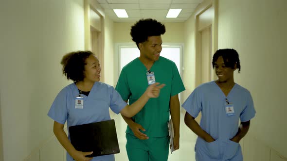 Three members of male and female doctors walking in hospital corridor talking, healthcare services