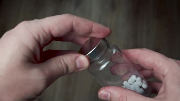 Male hands pour white pills from the meds bottle into the palm of the hand before taking them