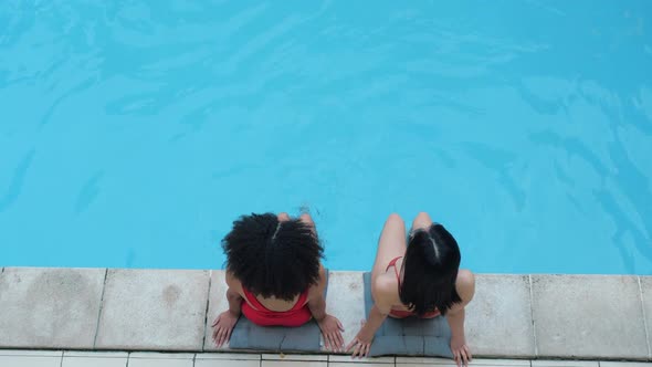 Two Black Haired Girlfriends Swing Legs in Water in Public Pool Relax Smile Look at Camera. African