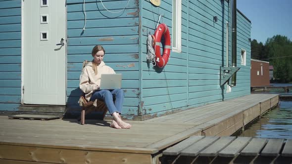 Alone Young Woman Typing on Laptop During Vacation Rest in Lodge Outdoors By River Spbd