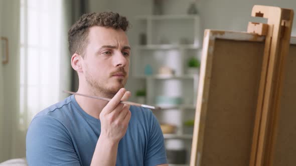 Young Man is Working in His Modern Home Studio in the Morning Drawing on Canvas Enjoying the Process