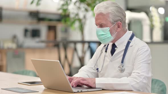 Senior Old Doctor with Face Mask Working on Laptop