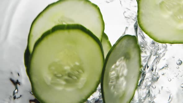 Thin Slices of Fresh Cucumber Fall Down Into Clear Water