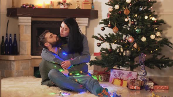 Young Positive Couple Sitting at the Christmas Tree on the Floor in the Room. New Year and Christmas