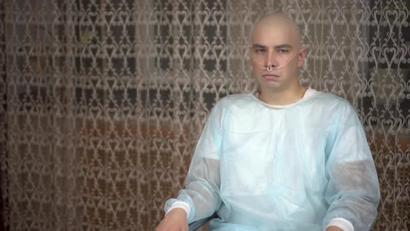 A Bald Young Man with Cancer Looks at the Camera and Cries. The Patient Covers His Face with His