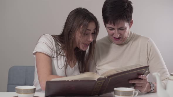 Portrait of Two Brunette Caucasian Women of Different Ages Watching Photo Album. Young-looking