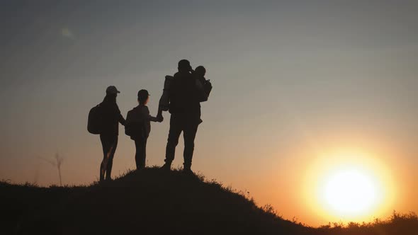 Silhouettes of Father, Mother and Children Hiking. Baby Sits on the Shoulders of His Father. Hiking