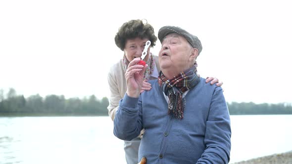 Senior couple in love blowing bubbles during a walk at the riverside