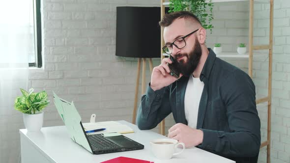 Handsome Bearded Man Drinking Coffee While Talking on a Smart Phone