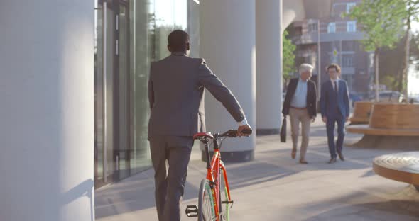 Follow Shot of African Businessman with Bicycle Walking Near Business Center