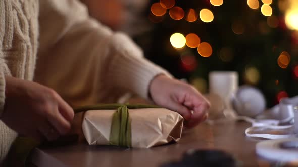 Closeup of Unrecognizable Young Woman Tying Ribbon on Wrapped Christmas Gift Box with Presents on