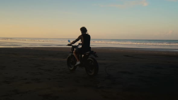 Motorcyclist Riding on Black Sand Beach at Sunset