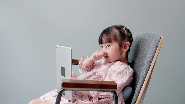 Asian child with fringe in hair sitting on chair laughing while using digital tablet.