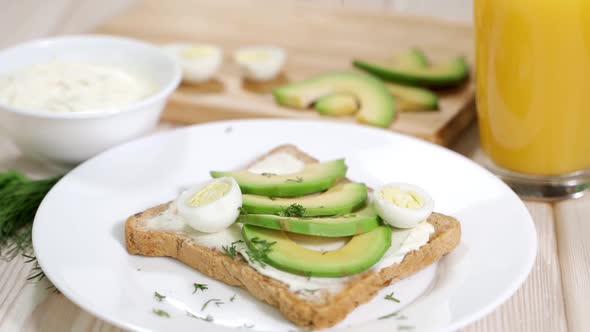 The Girl Is Preparing a Healthy Breakfast  Toasts with Avocado and Tender Curd Cheese Quail Eggs