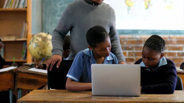 Male teacher using laptop with student in classroom 4k