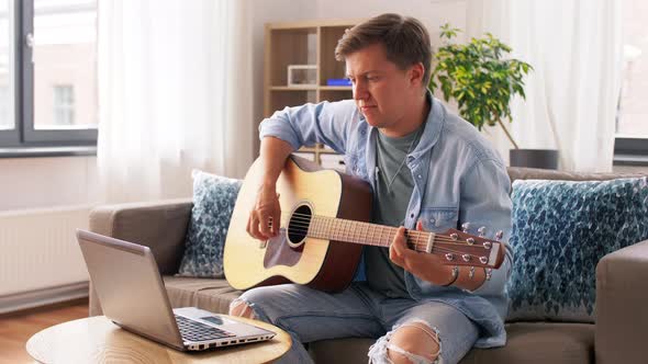 Young Man with Laptop Playing Guitar at Home