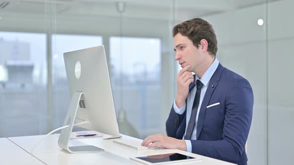 Young Businessman Thinking and Working on Desk Top in Office 