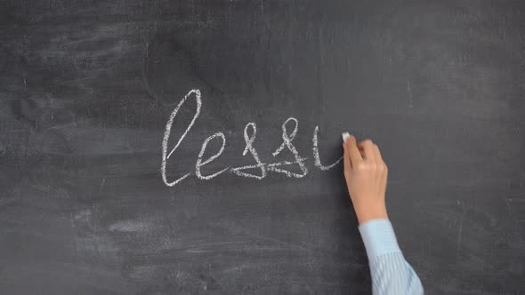 The hand of a female teacher writes the word LESSON on a black chalk board