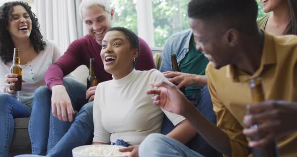 Diverse group of happy male and female friends watching sport drinking beer, cheering in living room